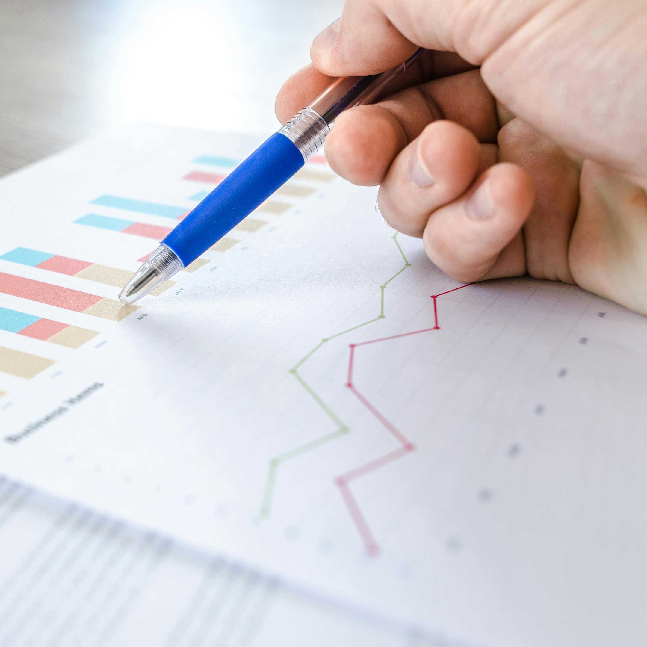 Image of a hand holding a blue pen pointing at financial data printed on a piece of paper